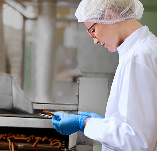 Frau mit roter Brille und blauen Einweghandschuhen in HACCP-Arbeitsschutzkleidung am Fließband