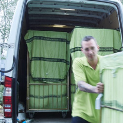 Mann schiebt Rollwagen mit abgeholter Wäsche von Transporter weg