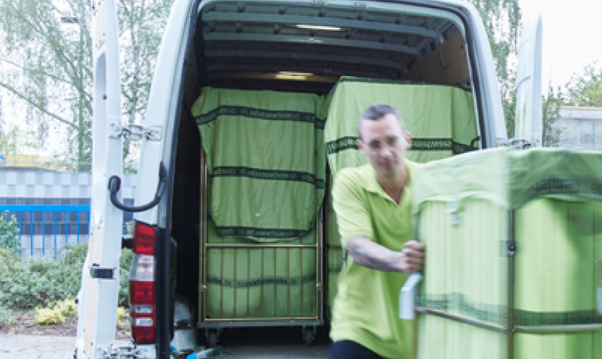Mann schiebt Rollwagen mit abgeholter Wäsche von Transporter weg