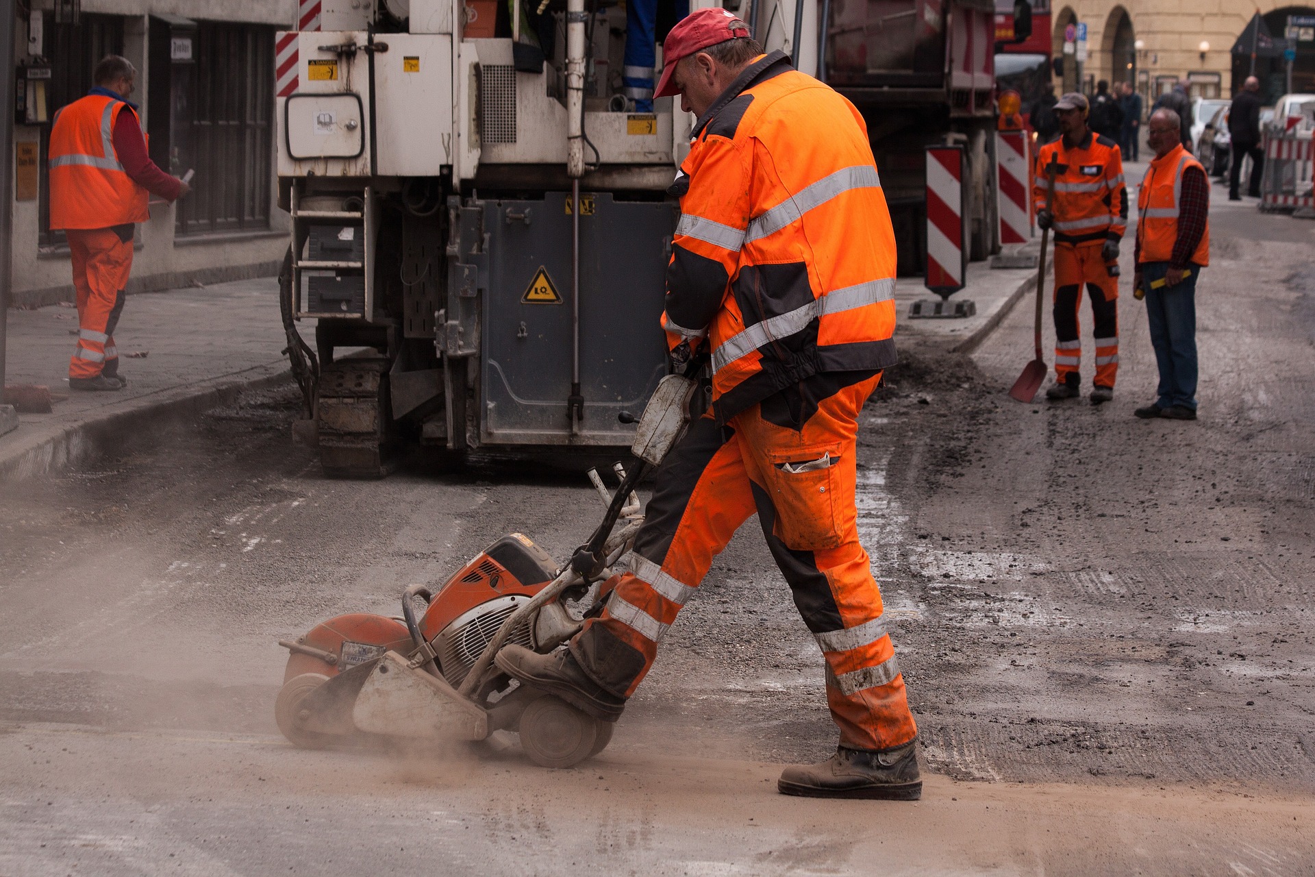 Arbeiter im Straßenbau, die Warnschutzkeidung tragen, im Vordergrund eine Person, die Teersäge bedient