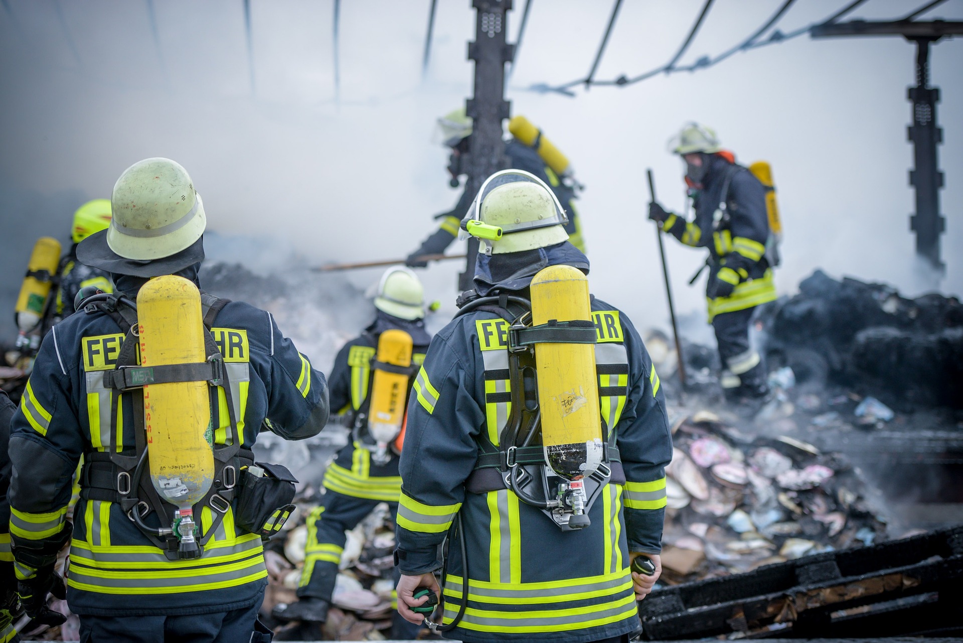 Feuerwehrleute in voller Montur (Warnschutzkleidung) auf dem Rasen vor einem Ziegelhaus