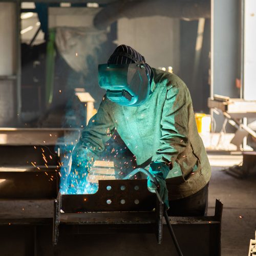 Schweißer in Schweißerschutzkleidung und Schweißmaske, der auf der Arbeit schweißt
