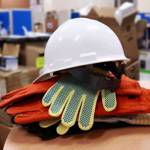 Ein weißer Schutzhelm, der auf aufeinander gestapelten Arbeitshandschuhen liegt, die auf einem runden Holztisch liegen