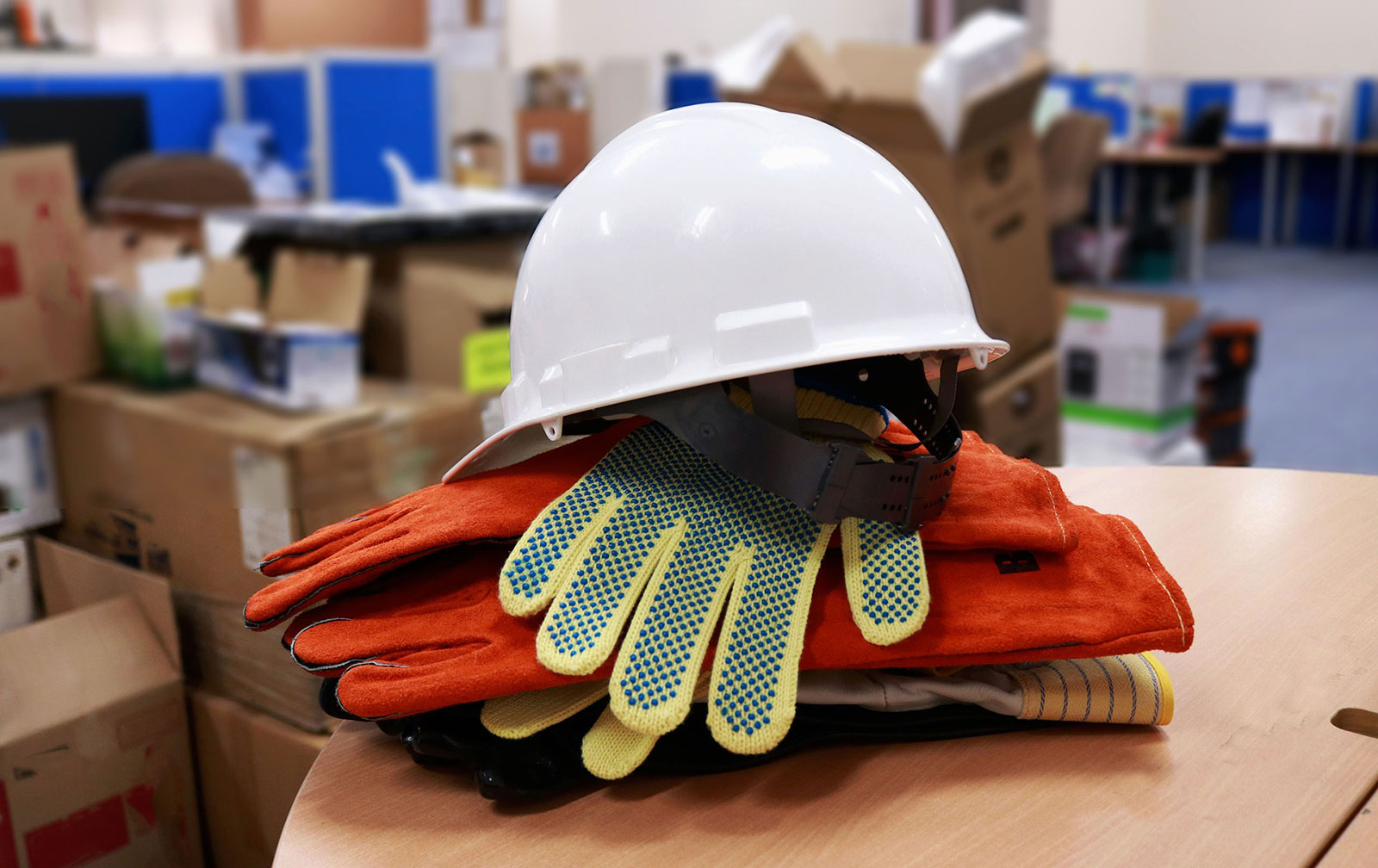 Ein weißer Schutzhelm, der auf aufeinander gestapelten Arbeitshandschuhen liegt, die auf einem runden Holztisch liegen