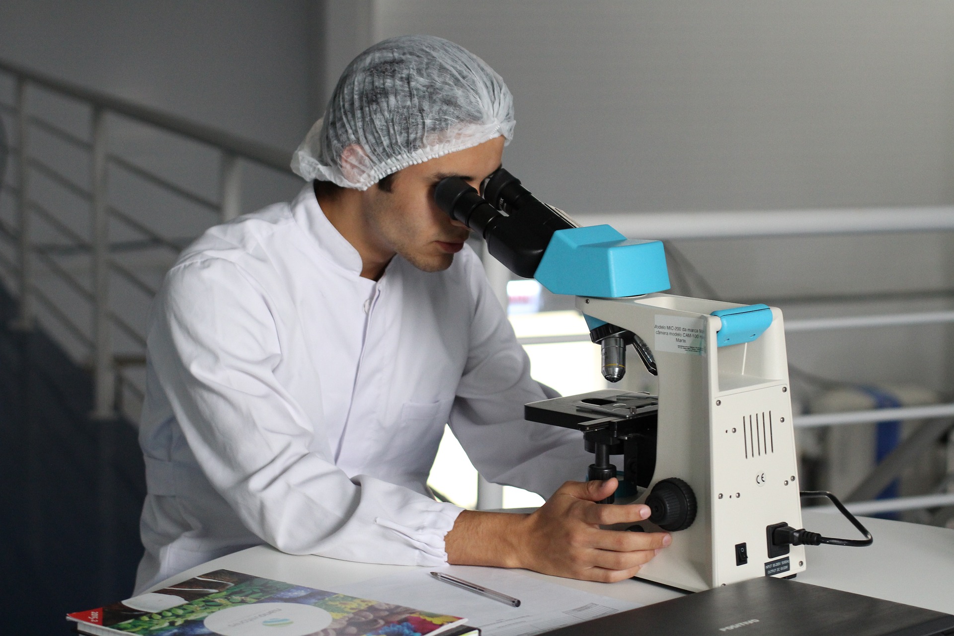 Apotheker, der Haarnetz und weiße Arbeitskleidung trägt und in ein Mikroskop schaut