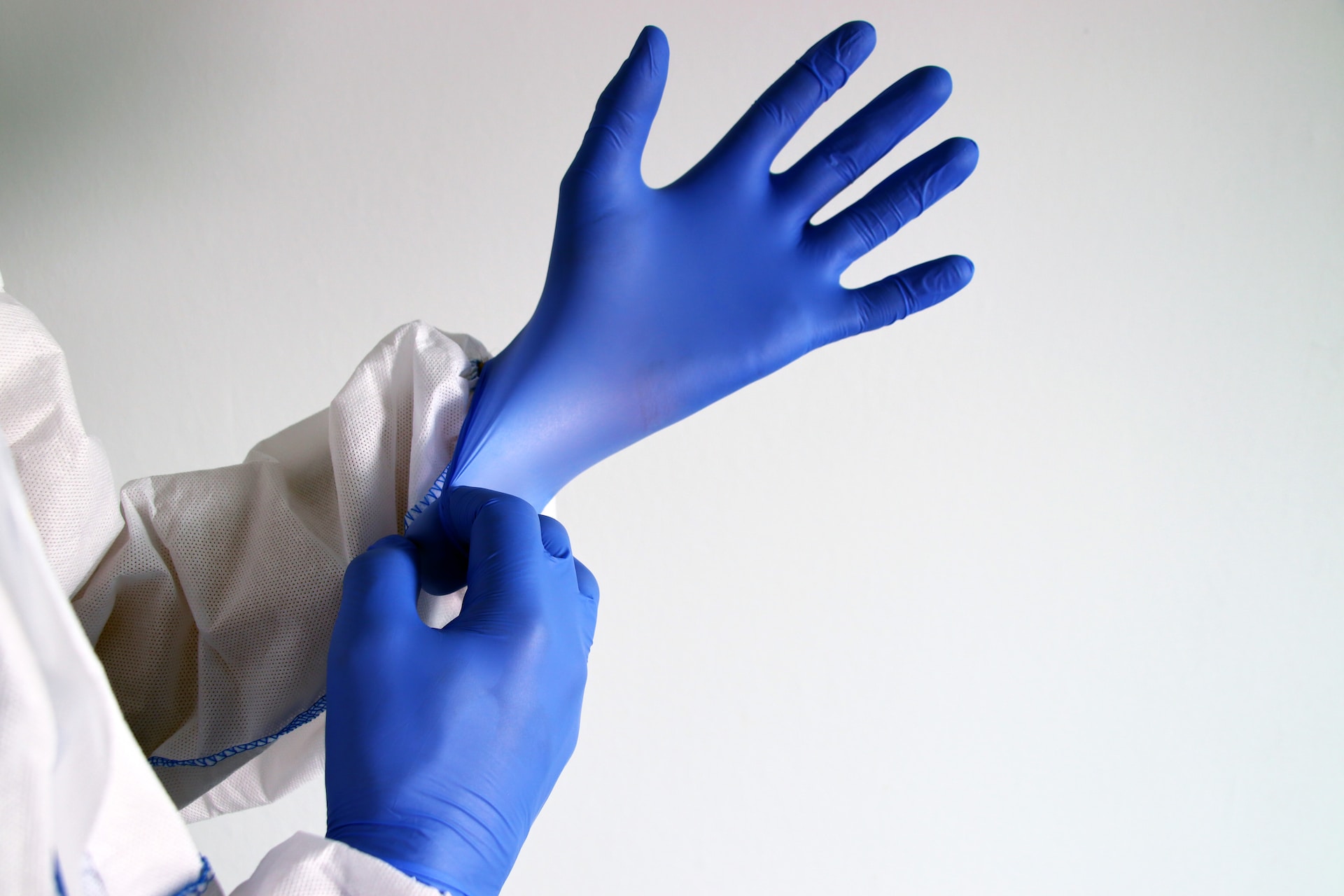 Fokus auf den Händen einer Person, die einen Schutzanzug trägt und sich gerade blaue Latexhandschuhe anzieht