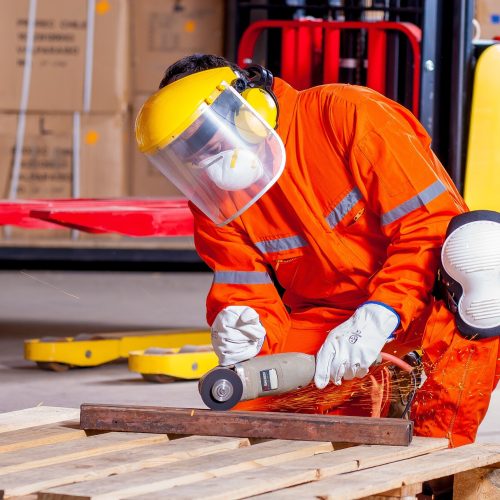 Person in Arbeitsschutzkleidung, Gehör- und Sichtschutz wie auch Mundmaske, die Metall flext