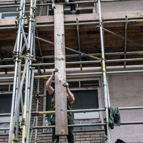 Arbeiter auf Baugerüst, die eine Holzplanke herunterreichen