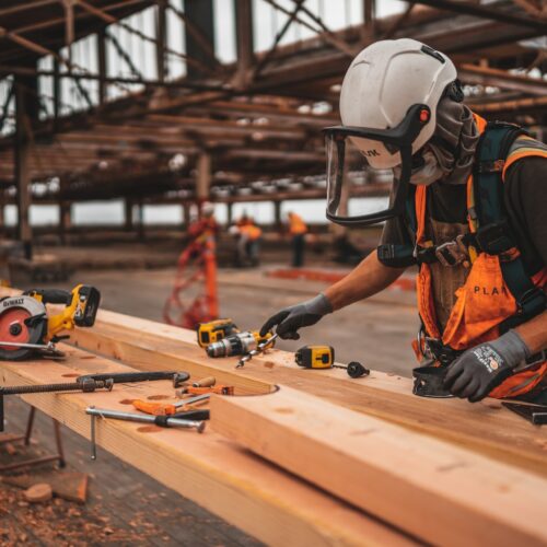 Arbeiter mit Schutzhelm, Handschuhen und Schutzvisier, der Holz bearbeitet