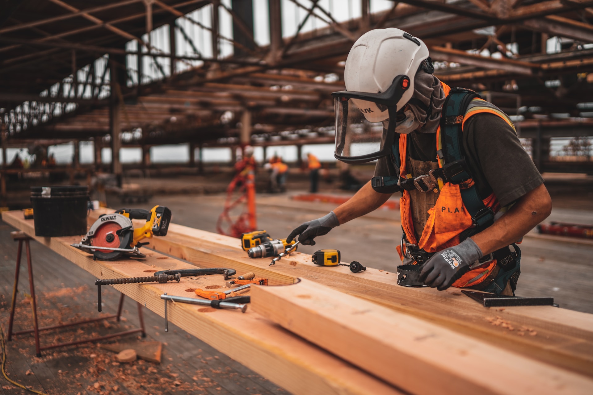Arbeiter mit Schutzhelm, Handschuhen und Schutzvisier, der Holz bearbeitet