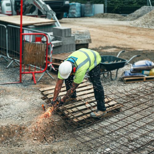Bauarbeiter mit Flex, der sich herunterbeugt, um zu arbeiten