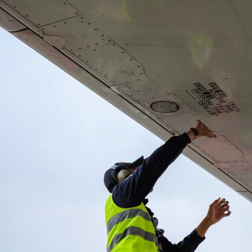 Flugzeugmechaniker überprüft Flugzeugflügel, trägt Gehörschutz und Warnschutzweste