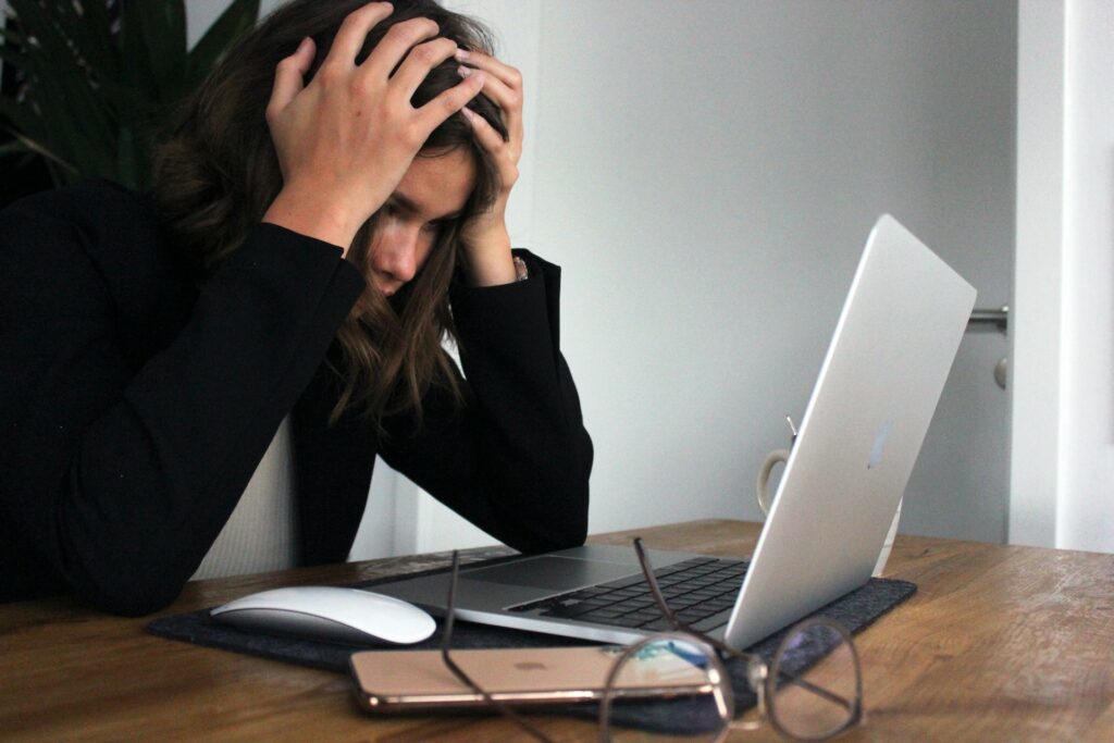 Frau, die vor Laptop am Arbeitstisch sitzt und sich die Hände an den Kopf hält