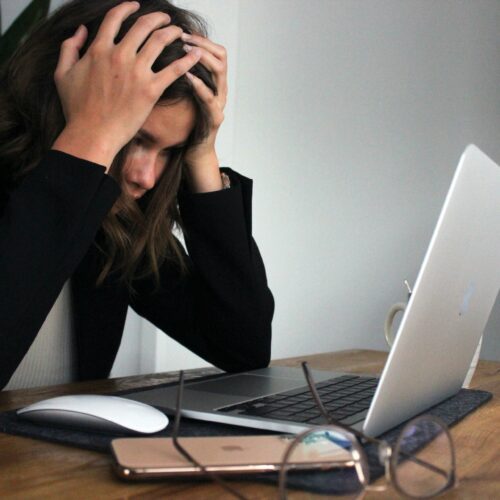 Frau, die vor Laptop am Arbeitstisch sitzt und sich die Hände an den Kopf hält
