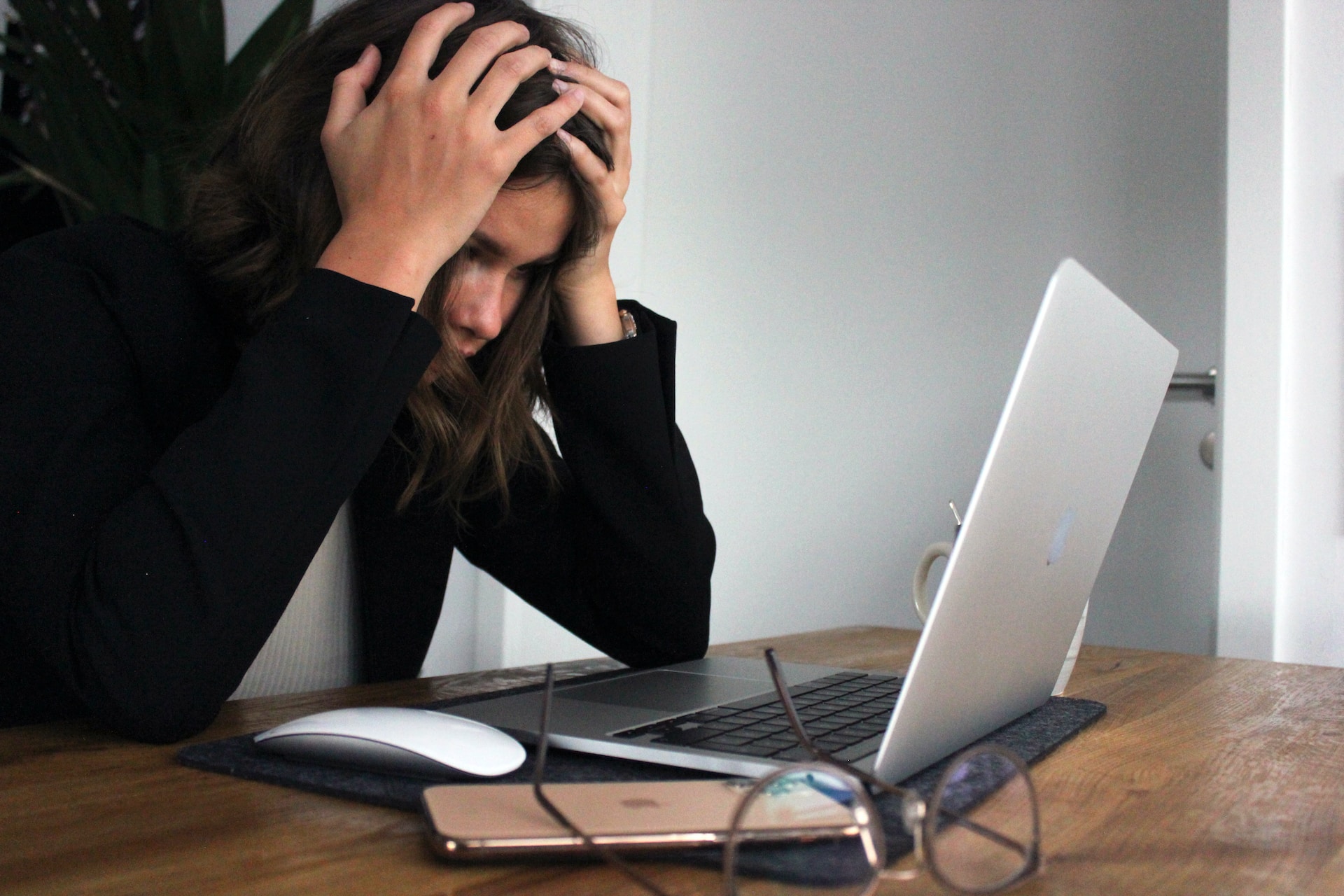 Frau, die vor Laptop am Arbeitstisch sitzt und sich die Hände an den Kopf hält