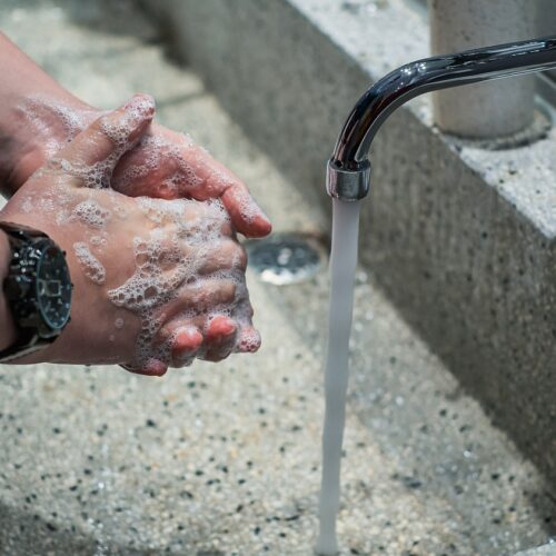 Hände werden gründlich mit Seife unter fließendem Wasser aus einem Wasserhahn gewaschen.