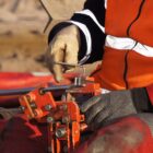 Arbeiter in Warnkleidung bedient eine manuelle Rohrbiegemaschine auf einer Baustelle.
