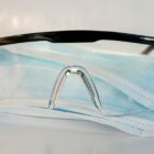 Schutzbrille liegt auf einer chirurgischen Maske auf einem weißen Untergrund.