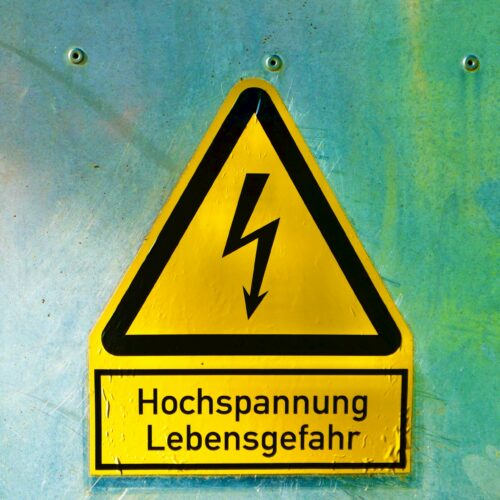 Warnschild mit Blitzsymbol und der Aufschrift "Hochspannung Lebensgefahr" an einer metallischen Wand.